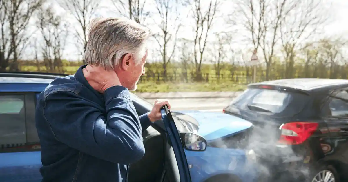 Driver holding neck and standing beside damaged car after collision — illustrating one of the common mistakes after a car accident, admitting fault or apologizing.