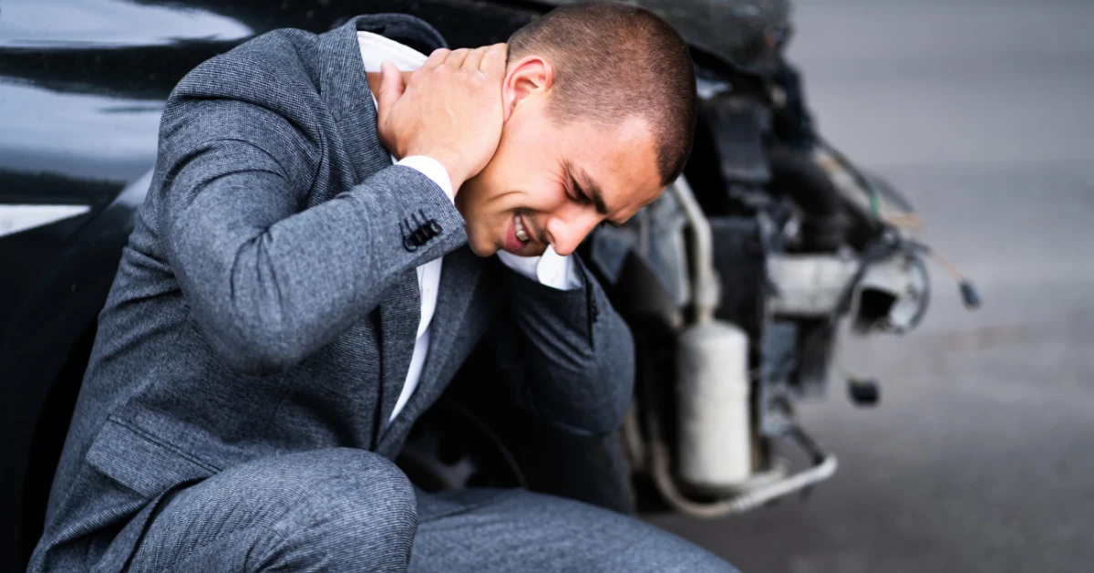 Man suffering from neck pain while sitting beside a damaged vehicle after a Portland car accident.