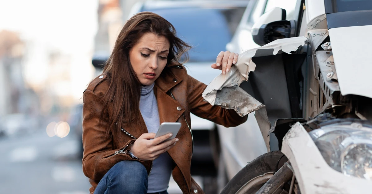 Driver documenting vehicle damage with a phone after being involved in a Salem car accident.