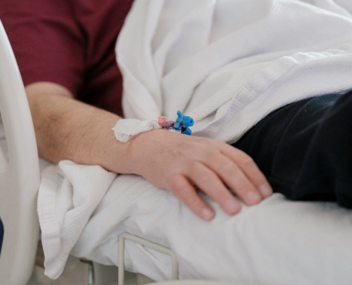 Hospital patient resting in bed with an IV catheter taped to the wrist after a serious medical error.