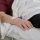 Hospital patient resting in bed with an IV catheter taped to the wrist after a serious medical error.