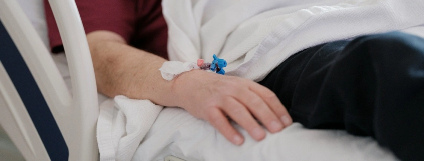 Hospital patient resting in bed with an IV catheter taped to the wrist after a serious medical error.
